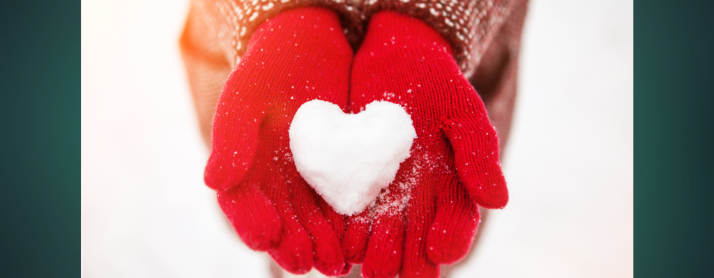 Red gloves holding snow in the shape of a heart.